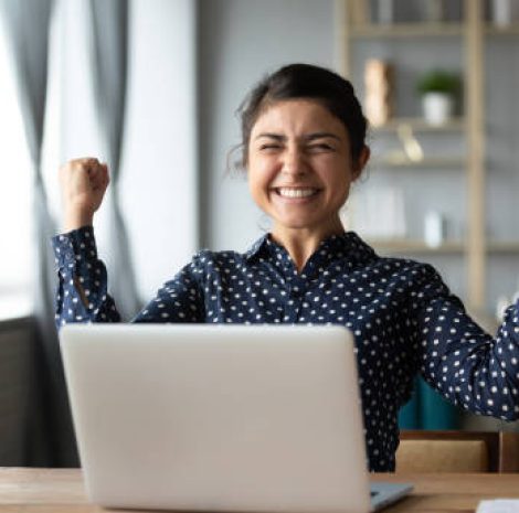 Euphoric young indian girl student winner celebrate victory triumph sit at home desk with laptop computer win online fortune feel excited get new job opportunity good exam result great news concept